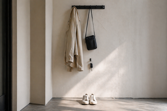 Wall-mounted hooks arranged vertically with jacket, bag, keys, and shoes showing movement-based organization flow in a minimal entryway